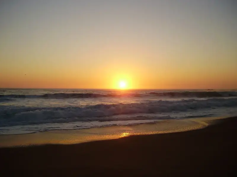 Pôr do sol dourado sobre o mar em Reñaca, com as ondas quebrando na areia
