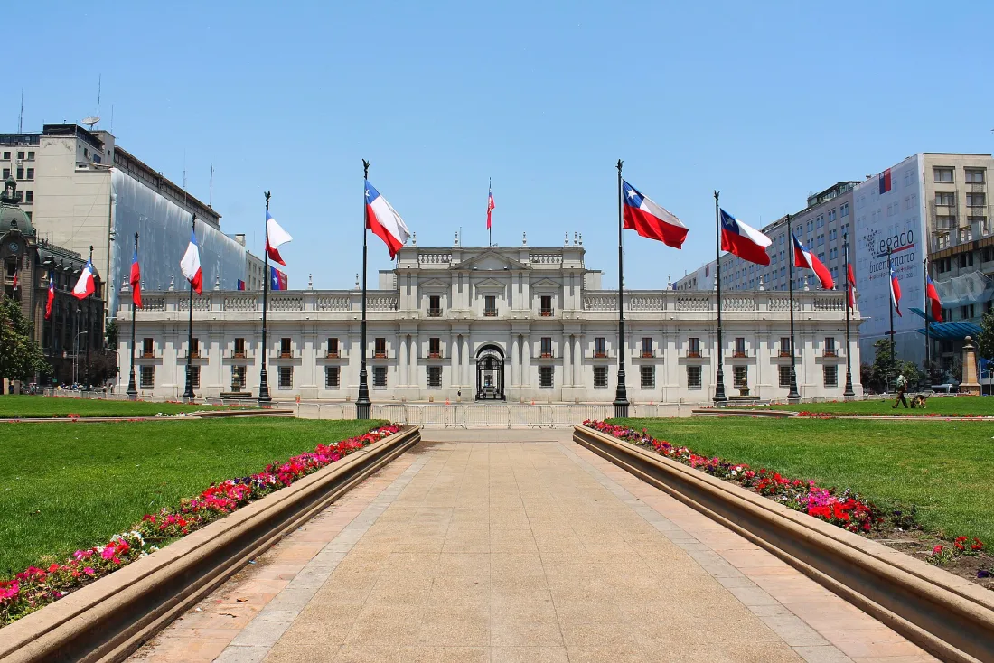 Palácio de La Moneda visto do jardim, com bandeiras do Chile hasteadas dos dois lados e canteiros de flores ao longo do caminho central