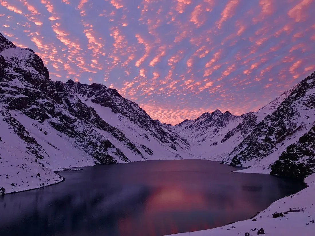 Pôr do sol rosado sobre a Laguna del Inca, em Portillo, com o lago escuro entre montanhas cobertas de neve