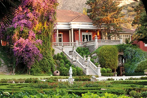 Casarão da vinícola Santa Rita entre buganvílias floridas e jardim de buxos aparados, com a escadaria de pedra ao centro