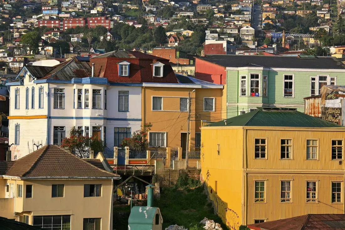 Casas coloridas de Valparaíso encaixadas umas nas outras na encosta do morro, sob a luz dourada do fim da tarde